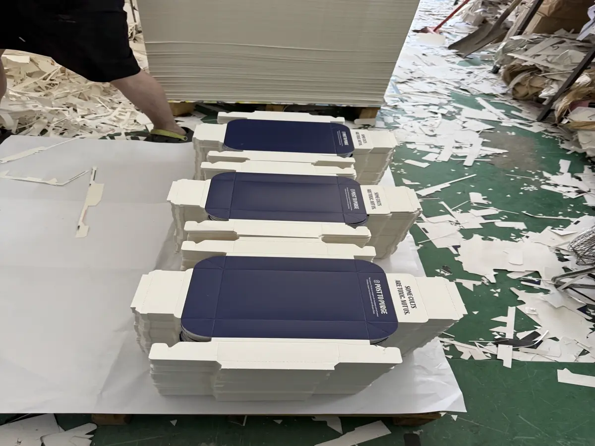 Stacks of printed product cartons on a packaging workshop table with paper offcuts nearby